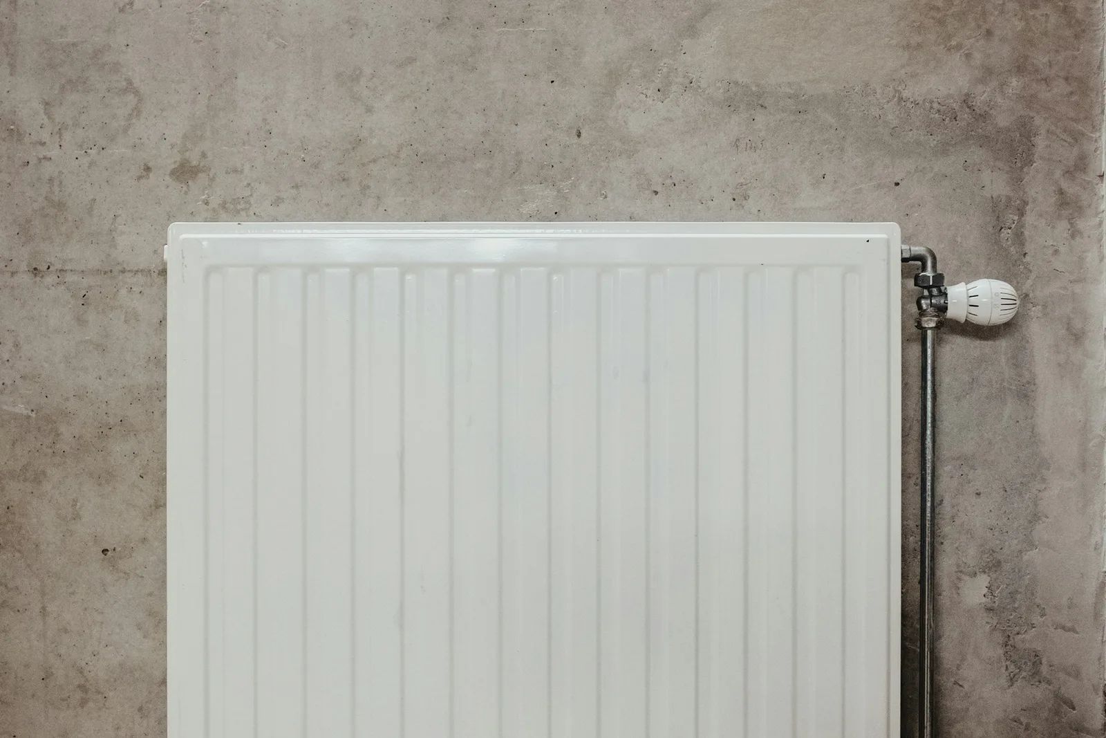 Weißer Heizkörper mit Thermostat vor einer Betonwand